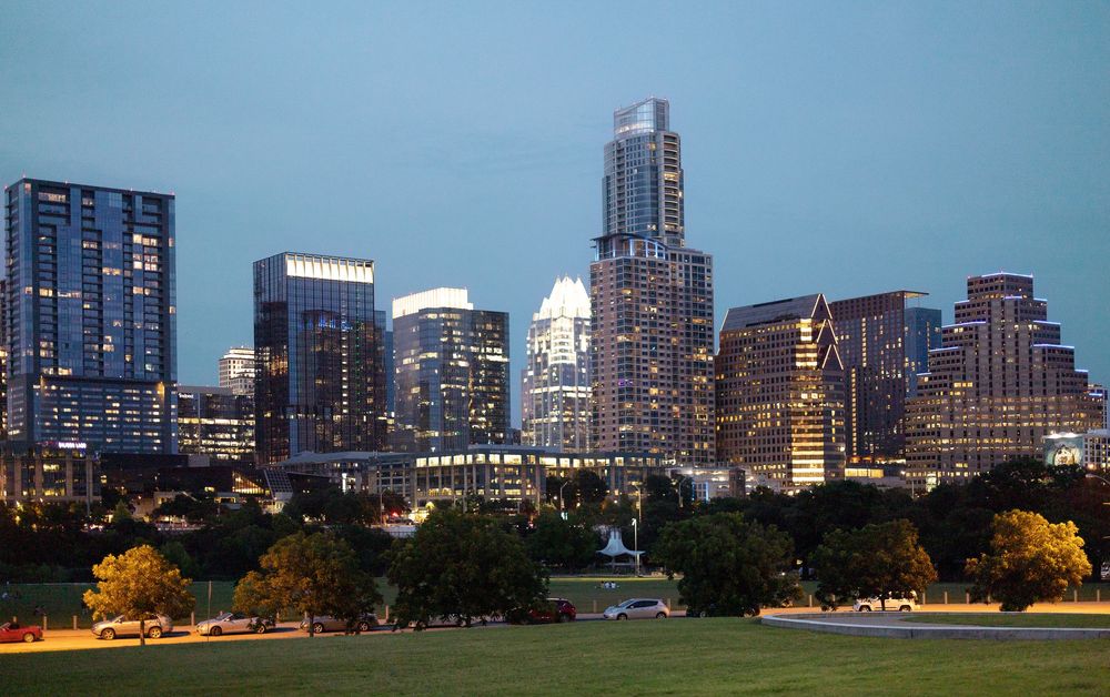 Austin Texas downtown skyline illuminated at dusk with modern skyscrapers reflecting city lights against a blue evening sky.