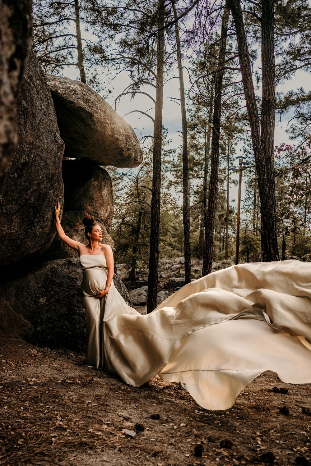White dress flows dramatically against forest backdrop with large boulder formation.