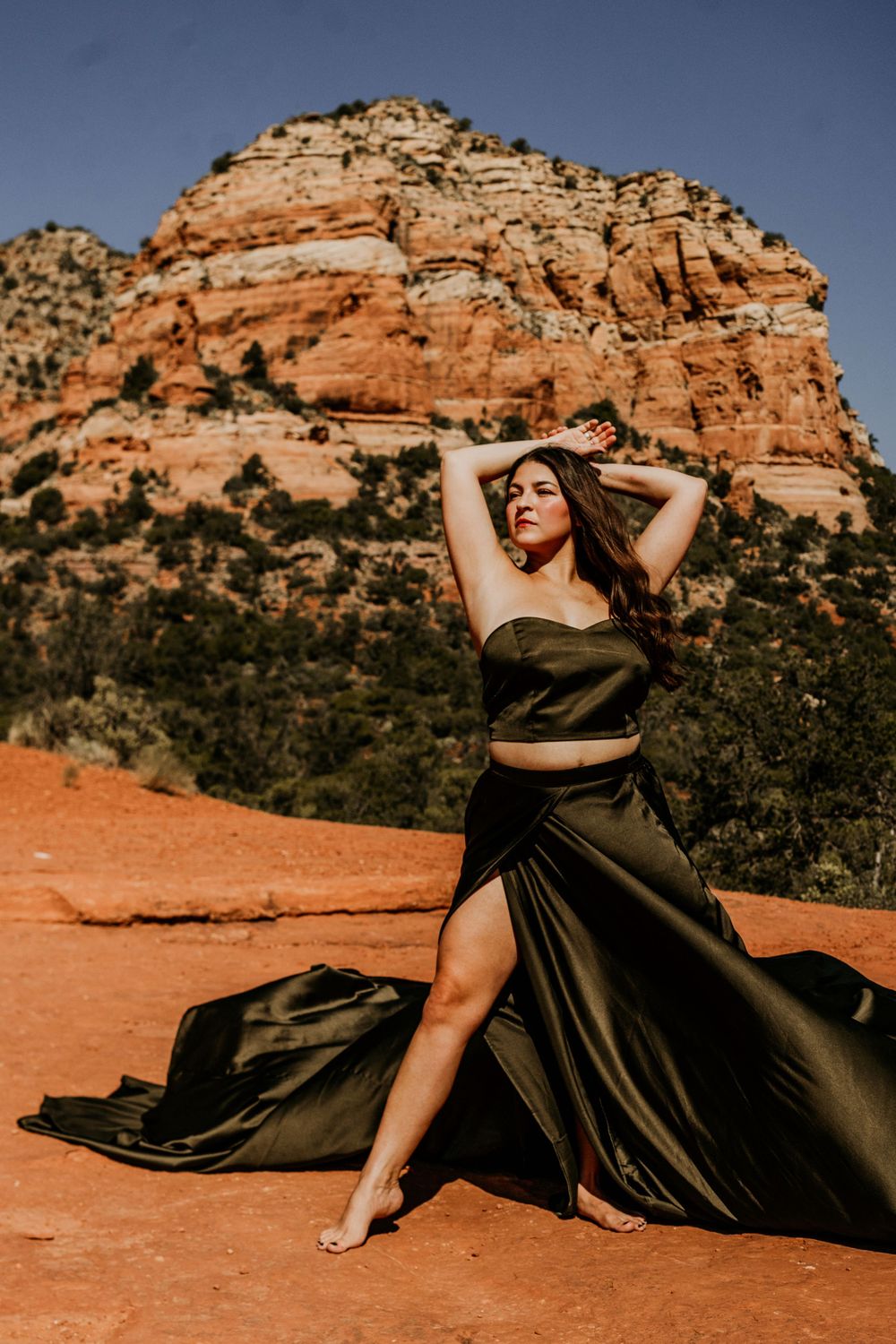 Olive silk dress flows dramatically against red rock cliffs in Sedona desert landscape.