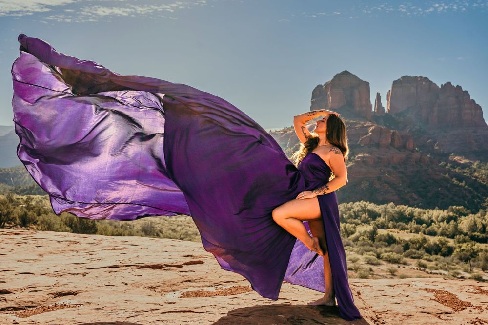 Flowing purple dress catches wind dramatically against Sedona's iconic red rock formations.