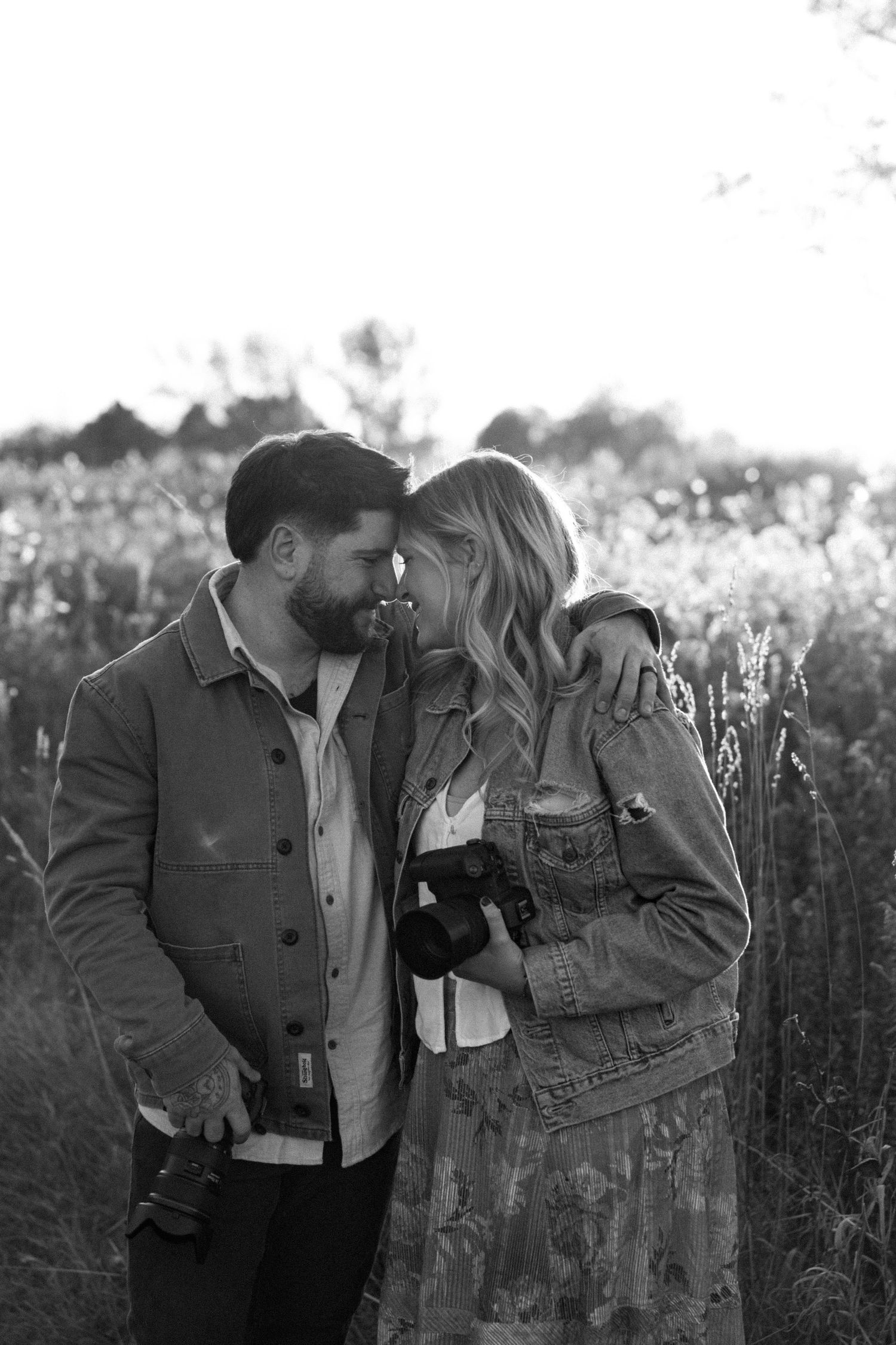 Romantic couple in casual attire sharing an intimate moment in a wildflower field at sunset.