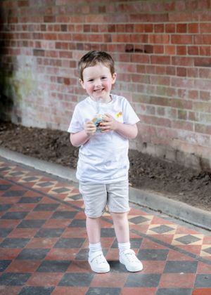Happy young boy in white t-shirt and grey shorts smiling on decorative tiled floor.