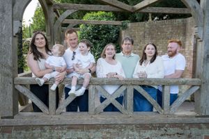 Happy extended family of seven posing together under rustic wooden pergola in garden.