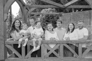 Black and white portrait of large extended family smiling together under wooden pergola.