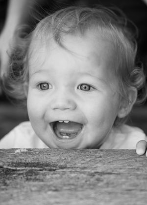 Black and white portrait of a joyful baby with curly hair and bright eyes laughing.