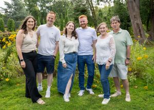 Group of six smiling adults posing together in a lush green garden.