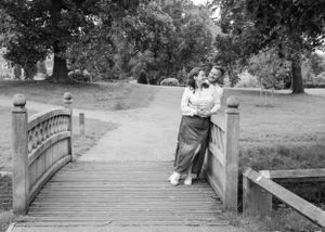 Black and white photo of a couple embracing on a wooden bridge in a park.