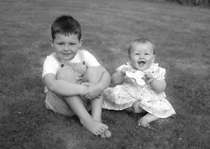 Black and white photo of a young boy and baby girl sitting on grass.