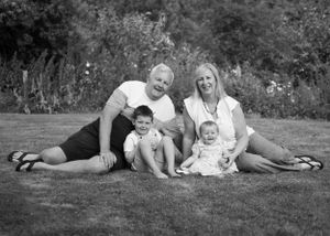 Black and white family portrait of parents sitting on grass with two young children.