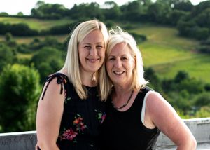 Two smiling blonde women posing together with rolling green hills behind them.