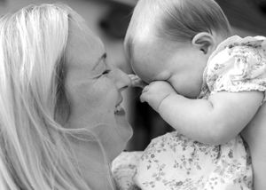Black and white close-up of a woman smiling at a baby she is holding.