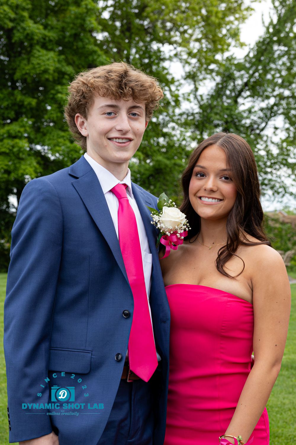 Formal couple at prom or dance event posing outdoors, wearing blue suit and red dress.