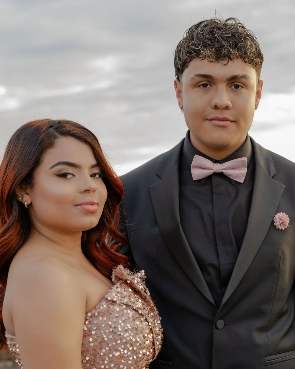 Couple in sparkly rose gold dress and black tuxedo pose for formal photos.