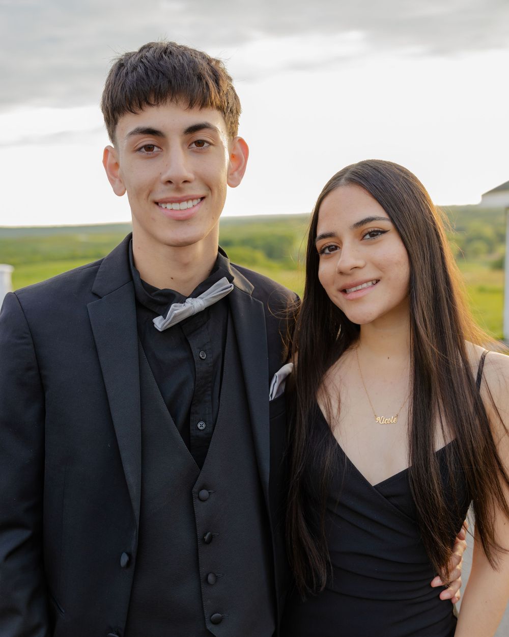 Couple in formal black attire smile together during outdoor photo session.