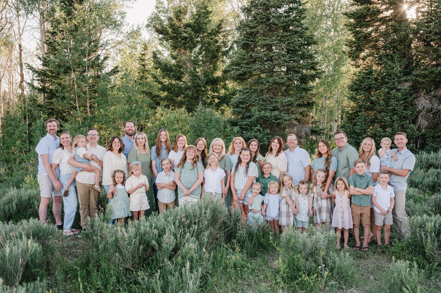 Large family group portrait in coordinating outfits against mountain forest backdrop.
