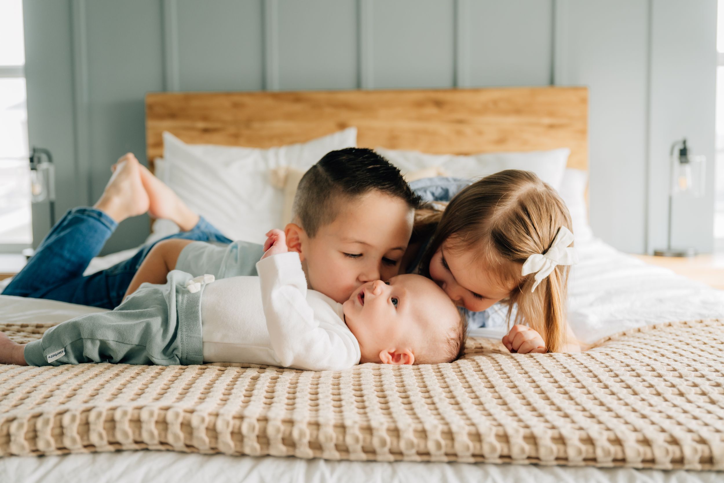 Children laying together on a cozy cream-colored knit blanket on a bed sharing a sweet moment.