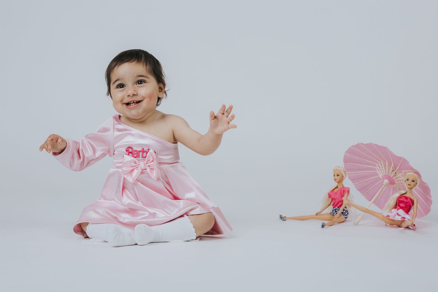 A pink dress contrasts with a white background as dolls rest nearby.