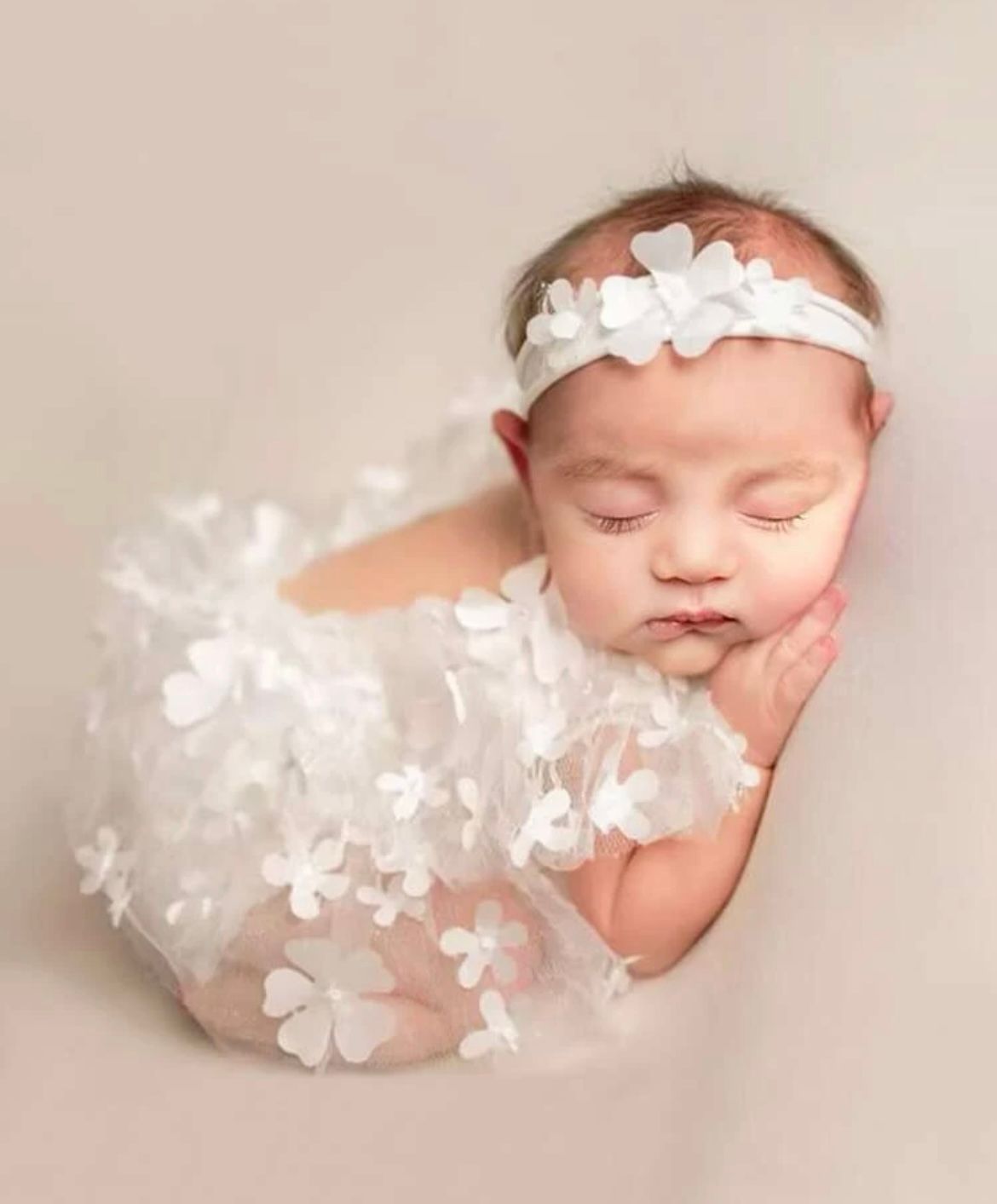 Newborn photography session with delicate white floral decorations and soft pink tones.