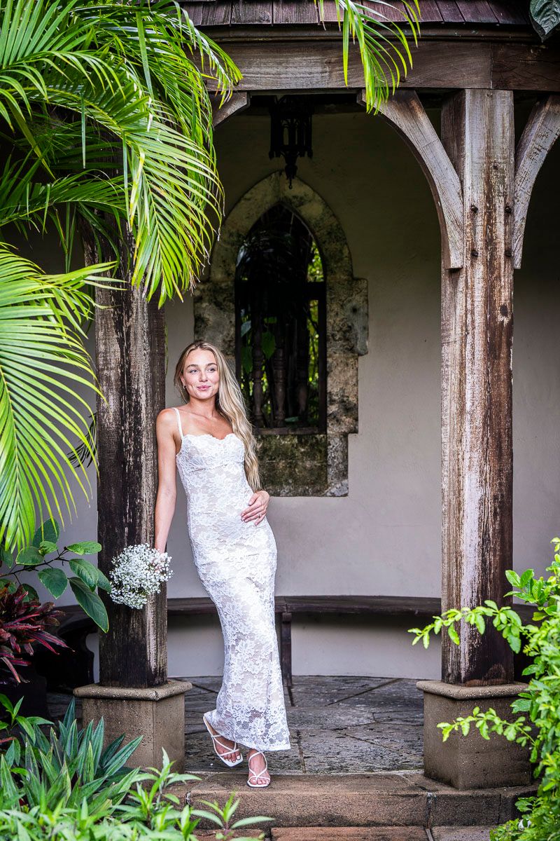 White lace dress against tropical garden architecture with palm fronds and stone pillars.