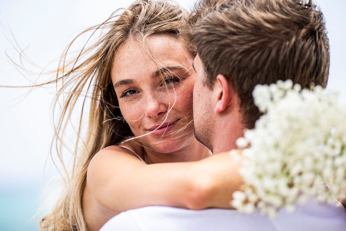 Romantic embrace with white flowers against ocean backdrop.