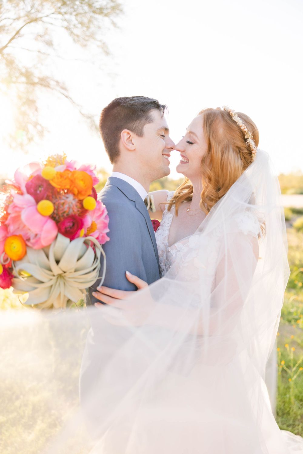 An intimate moment between newlyweds with flowing veil and colorful bouquet in golden light.