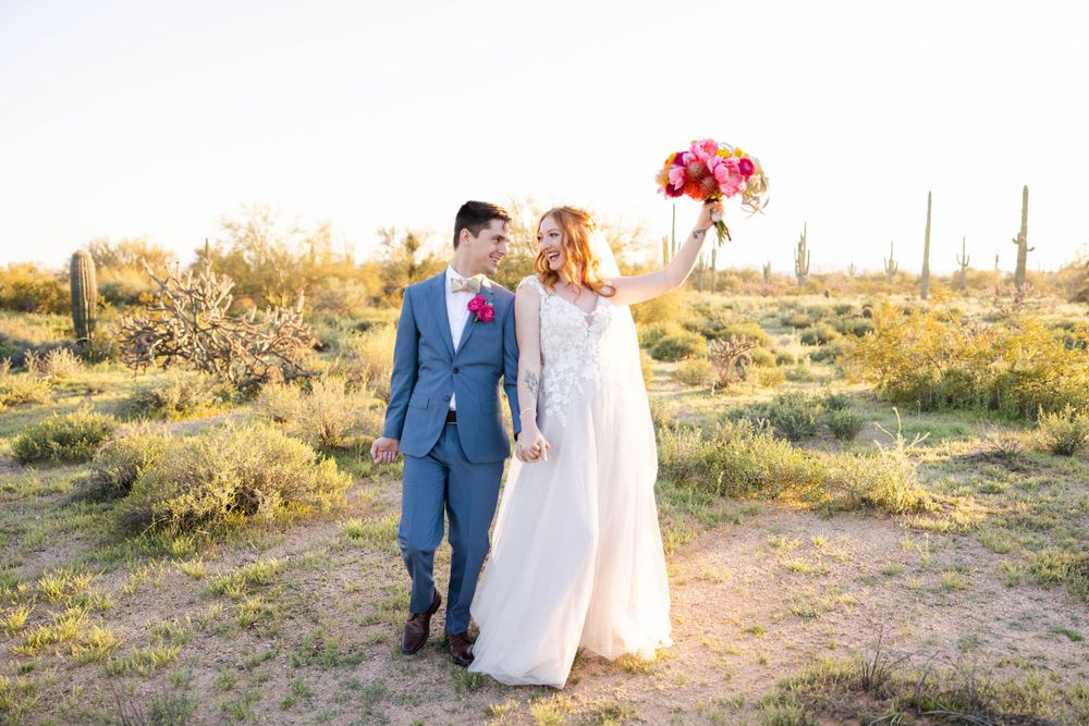 A joyful couple walking hand in hand through a desert landscape with cacti and golden sunlight.