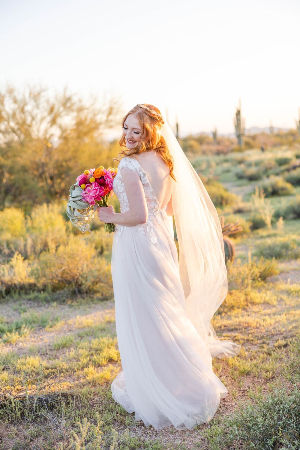 Ethereal bridal portrait in desert setting with flowing veil and vibrant bouquet.