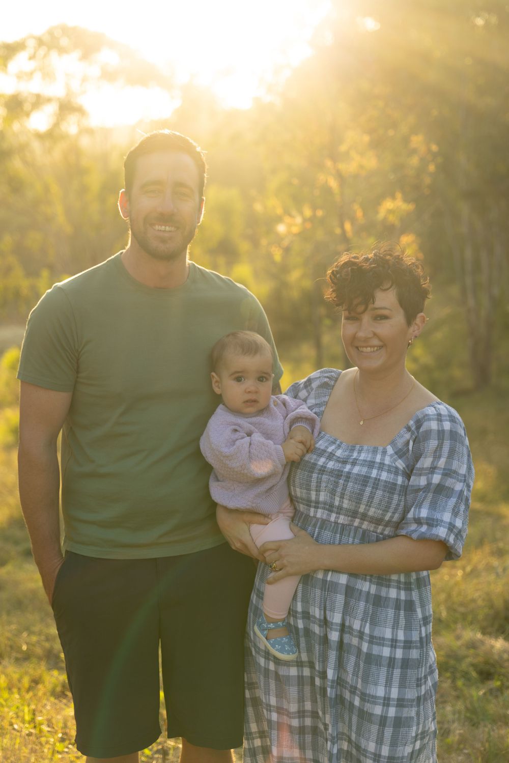 A warm sunset photo of a family standing together in a grassy field.