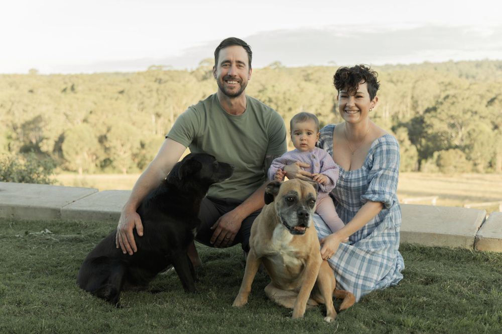 Family relaxing together on grass with their dog and baby during an outdoor photoshoot.