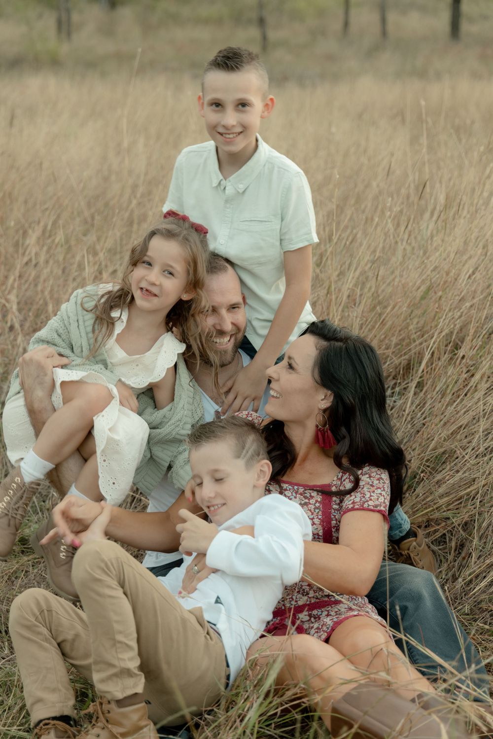 Family sitting together and sharing laughs in a rustic field setting.