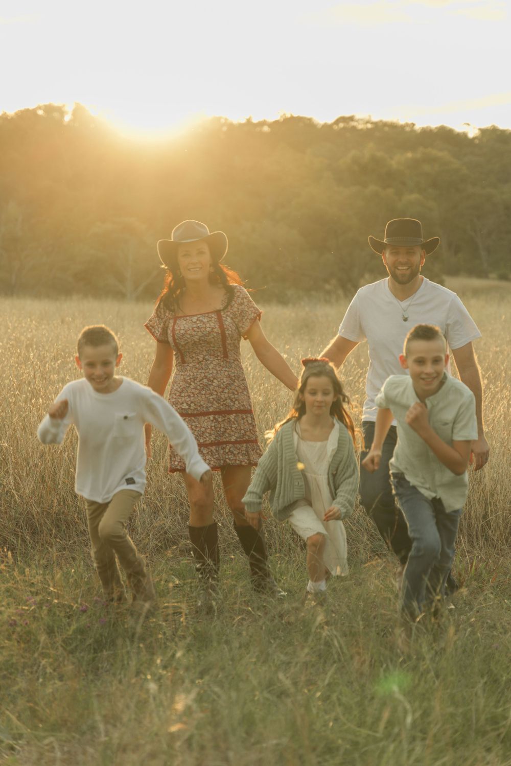 Playful family group running and laughing together in tall grass at sunset.