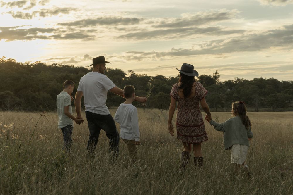 People walking together across an open field against a dramatic sunset sky.