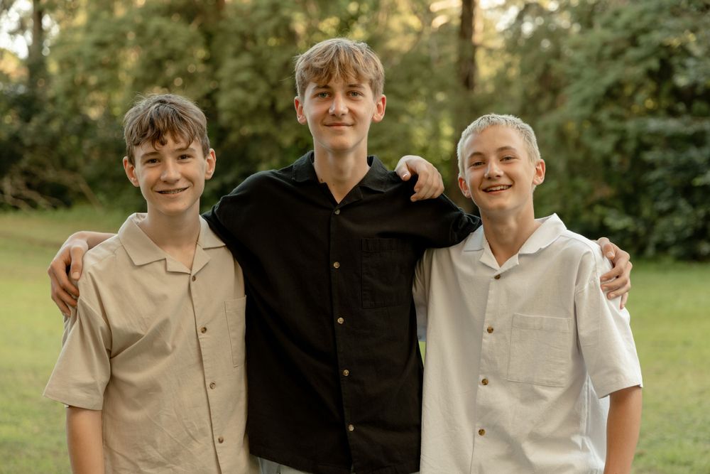 Three brothers posing together outdoors wearing casual attire.