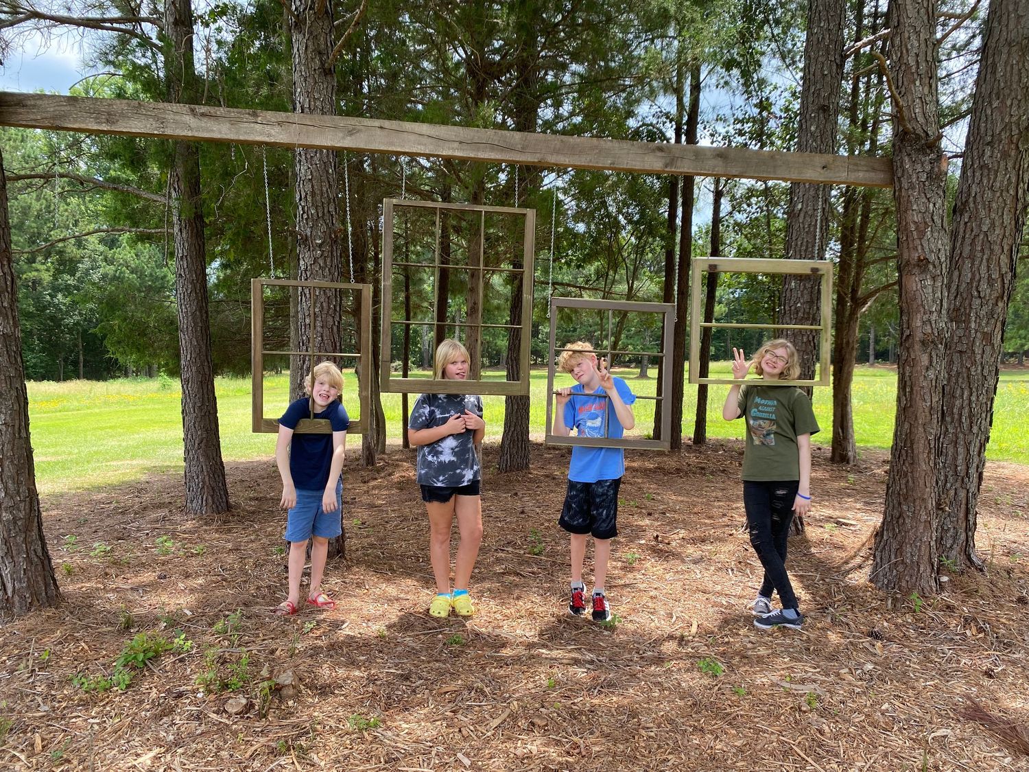 Hanging wooden frames in small wooded area in field with kids making silly faces