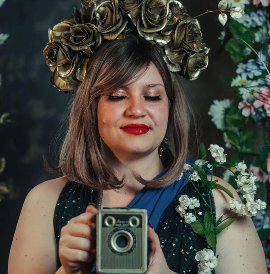 Portrait of creative photographer with flower crown holding vintage camera.