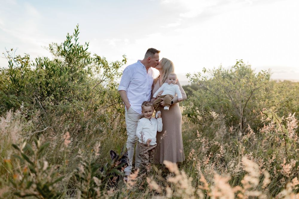 A tender family moment shared in a sunlit field of tall grass and shrubs.