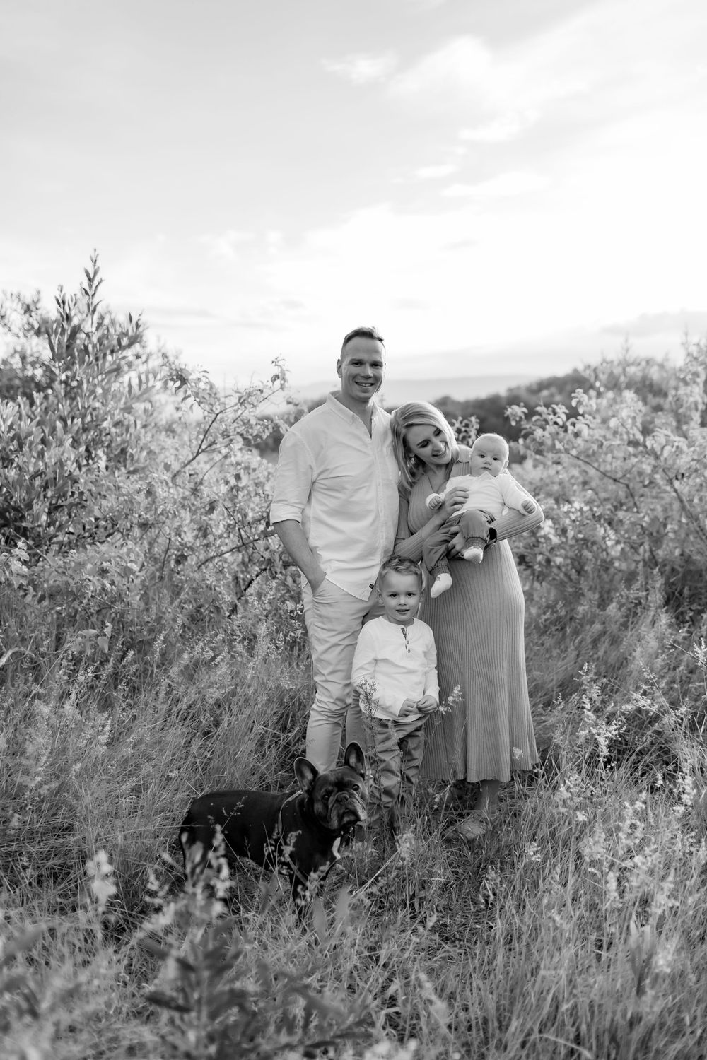 Black and white outdoor family portrait in tall grass with dog.