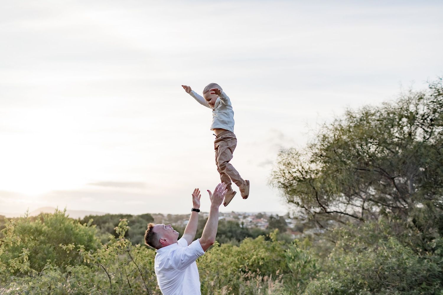 Joyful outdoor scene of lifting and playing in a natural setting at sunset.