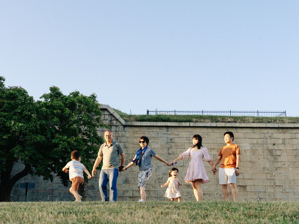A group of people joyfully running and jumping together along a stone wall with green trees in the background at Boston Castle Island.
