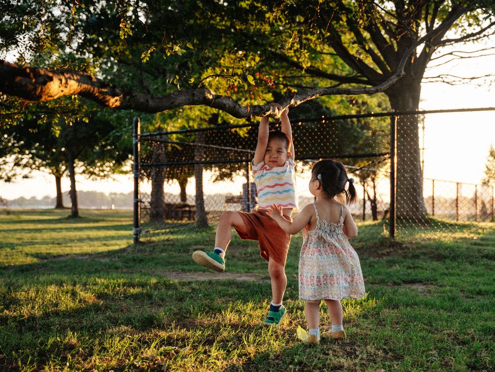 Two friends enjoy playing on a rope swing at sunset in a grassy backyard with golden sunlight filtering through trees at Boston Castle Isl.