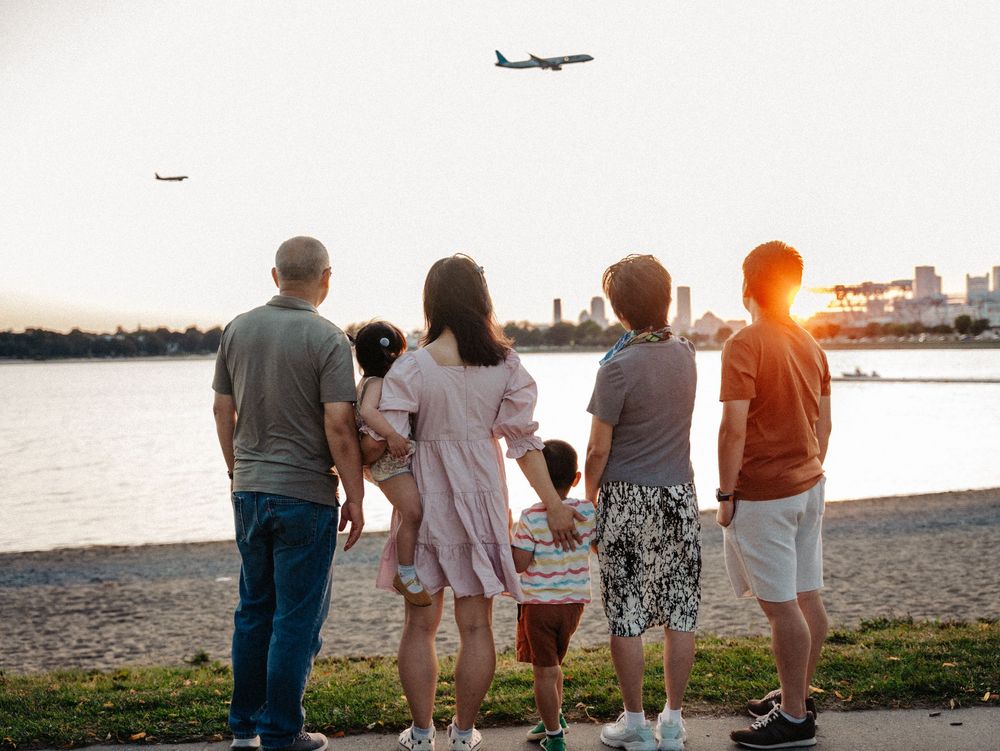 Group watching airplane at sunset from waterfront park with urban skyline in background at Boston Castle Island.