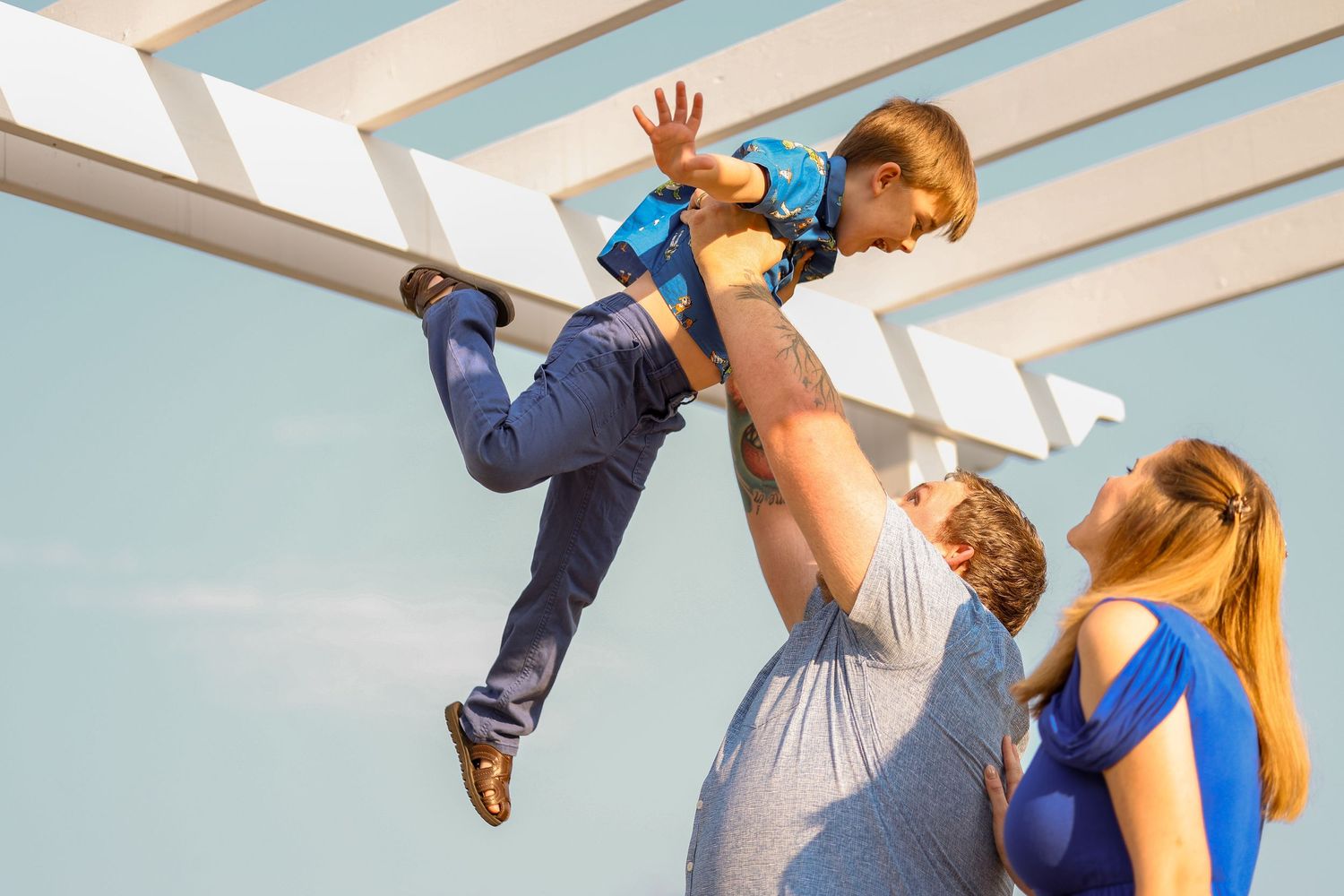 Playful moment as a young child is lifted high in the air against a white pergola backdrop.