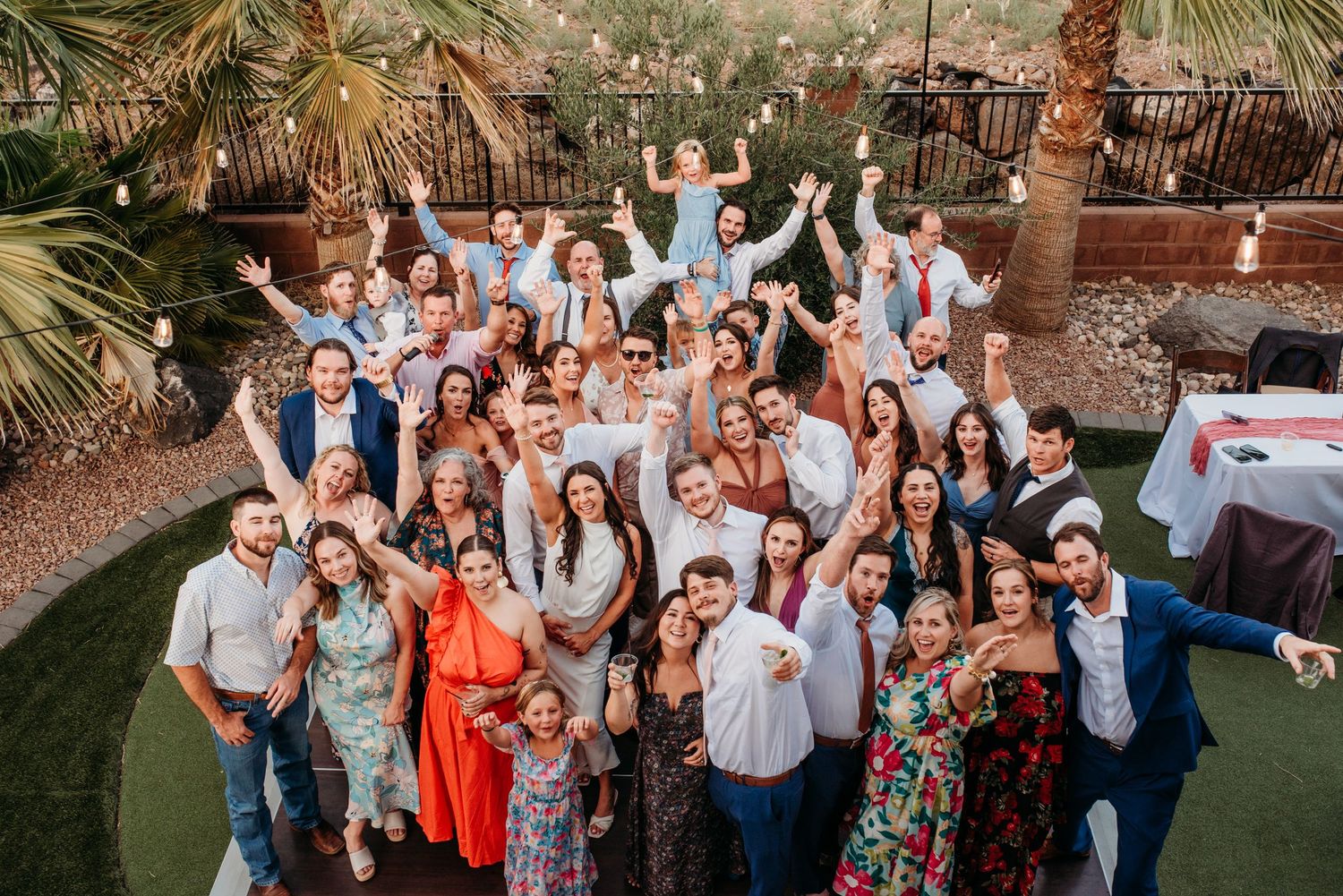 Large group photo of wedding guests posing together at an outdoor venue with palm trees.