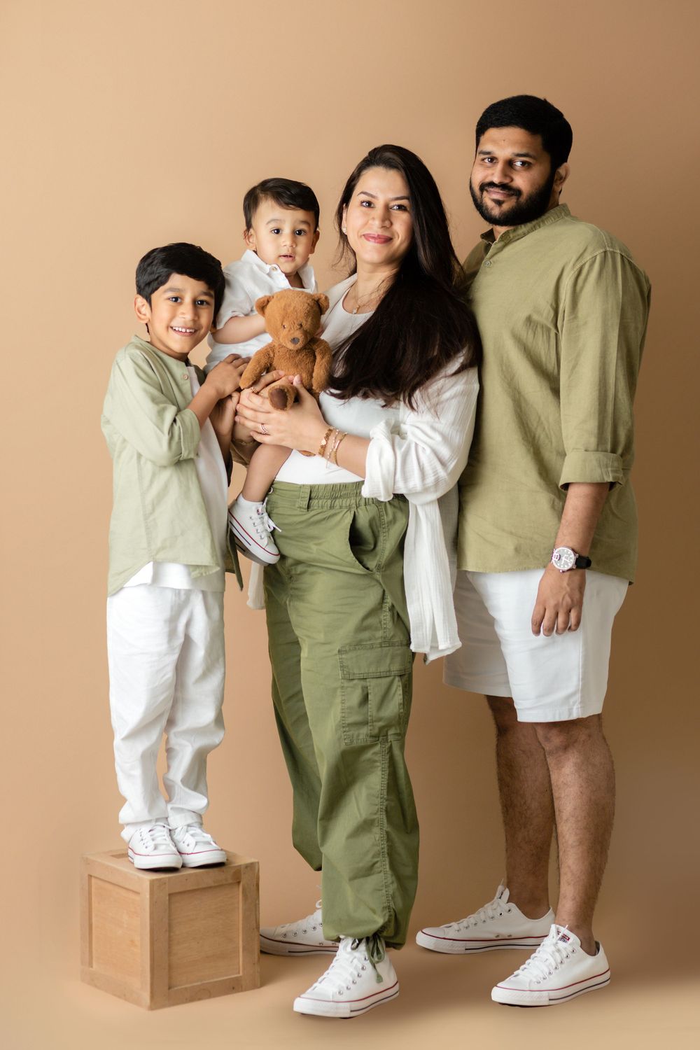 Modern family portrait in coordinated white and olive outfits against neutral backdrop.