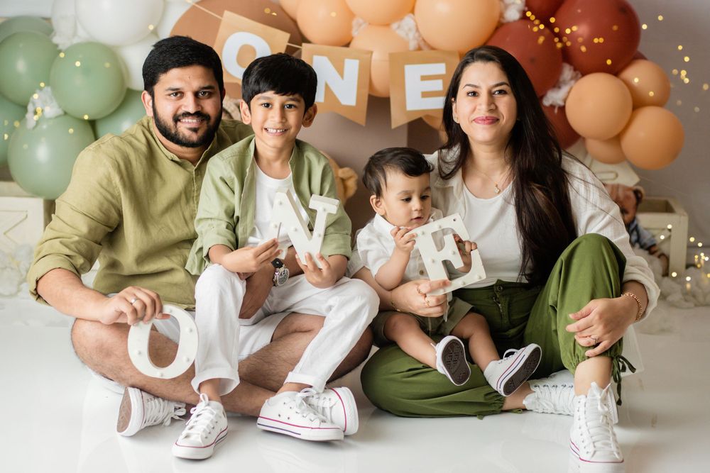 Family portrait with balloon arch and 'ONE' banner in modern white and neutral tones.