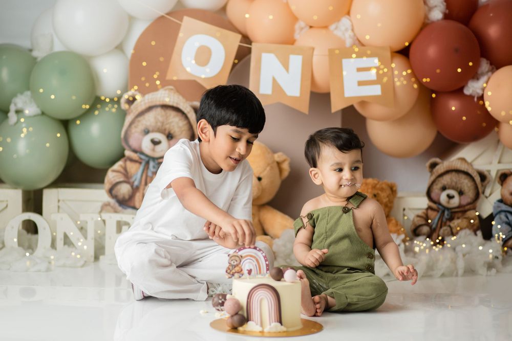 Two children sitting by a cake at first birthday party with balloon decorations.