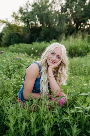 A person with blonde hair laying in a green summer meadow wearing a blue top.