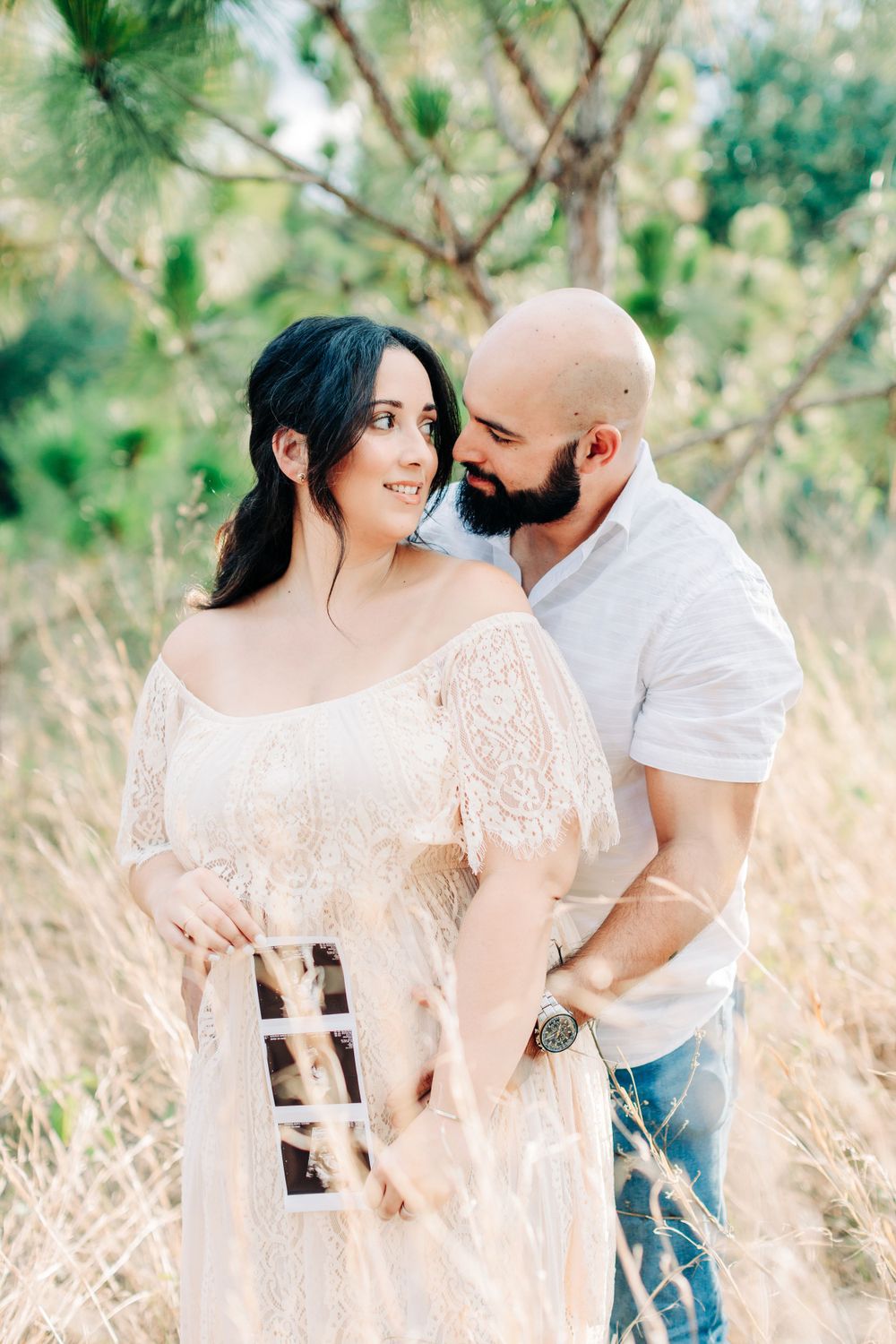 Intimate moment between mom and dad to be in the tall grass field holding an ultrasound scan