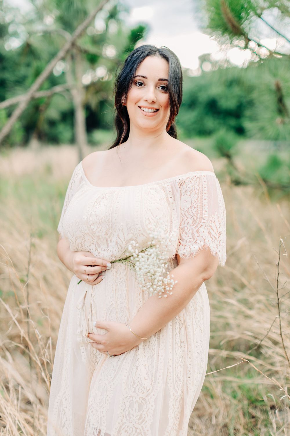 Pregnant mom holding baby breath flowers near her belly in a filed with tall grass in Orlando
