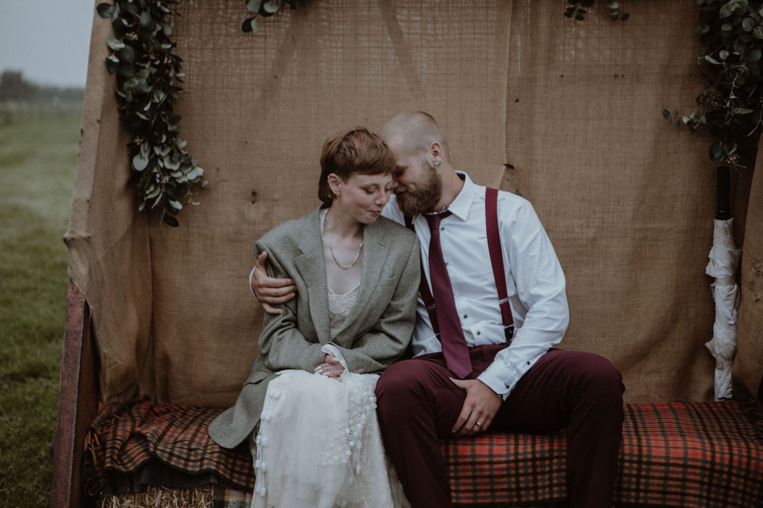 A vintage-inspired wedding scene with a couple sitting close on a decorated rustic bench.